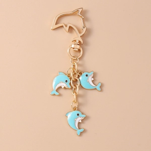 Detail of creative golden dolphin keychain with blue and white enamel charms on beige background
