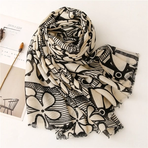 Lightweight black and white floral cotton-linen scarf with fringed edges on a desk