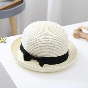 Detailed weave of cream kids straw hat featuring a black ribbon bow on white tabletop