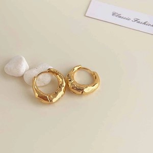 Detail shot of golden hoop earrings with unique irregular lava texture and metal finish