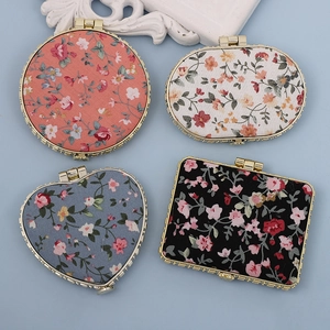 Floral fabric pocket mirrors in round, heart, and oval shapes with gold metal frames