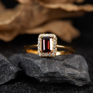 Macro shot of gold S925 ring with garnet stone and white gems on a dark stone background