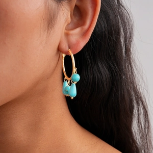 Close-up of gold hoop earrings with turquoise stone tassels worn by a model