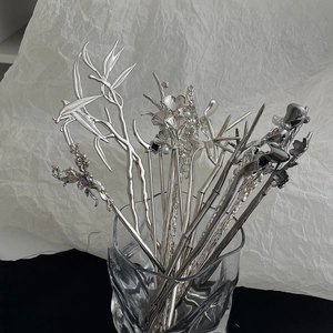 Detail view of silver metal hairpins with bamboo and floral motifs in a glass vase