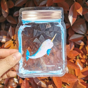 Detail of mason jar suncatcher with narwhal decal held against autumn leaves