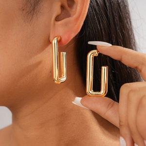 Close-up of geometric golden rectangular hoop earrings worn by a model in a minimalist style
