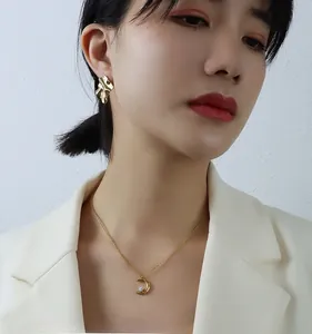 Nahaufnahme einer 18K Gold Mondkette mit Zirkon und unregelmäßigen geometrischen Ohrringen
