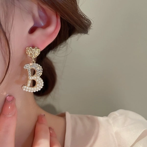 Primo piano dell'orecchino a cuore e pendente a B con perle e cristalli su una modella