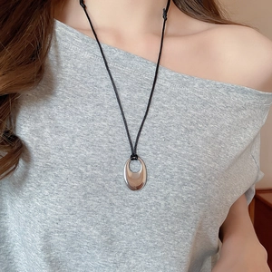 Vue macro du pendentif ovale argenté sur un collier en cordon noir porté par un mannequin