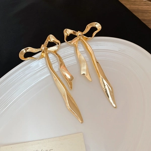 Élégantes boucles d'oreilles nœud dorées avec pompons présentées sur une assiette en céramique