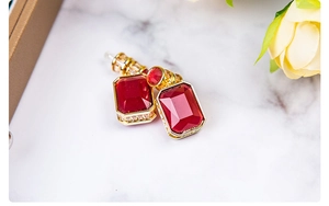 Detail of long geometric earrings with rectangle red gemstone and gold setting