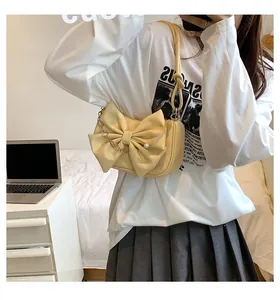 Detail of yellow underarm bag featuring a large bow and decorative pearl chain strap