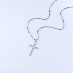 Detail of a silver double-layered hollow cross pendant with a box chain on gray background