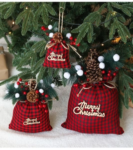 Three sizes of red and black plaid Christmas gift bags with pine cones and berries