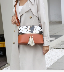 Detail of fashion cow print and brown leather shoulder bag with decorative tassel