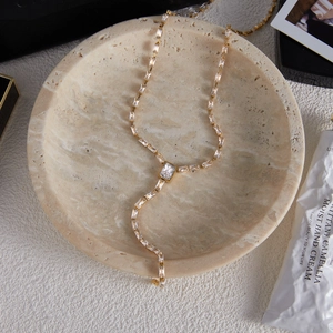 Détail de collier en Y doré avec pierres de zircon rectangulaires sur plateau en pierre