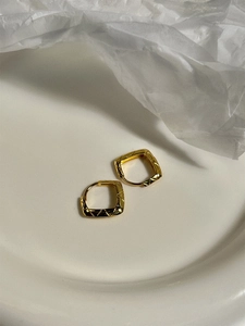 Macro view of gold quilted square hoop earrings in a white ceramic tray for a chic look