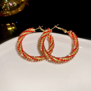 Detailed macro view of twisted hoop earrings with red and gold pavé crystals on white tray