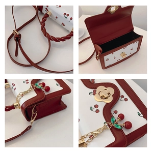 Detail showing red edge stitching, metal lock, and cherry pendant on a white crossbody bag