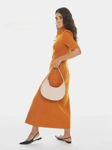 Detail of a chic cream-colored leather half-moon handbag held by a model in a long dress