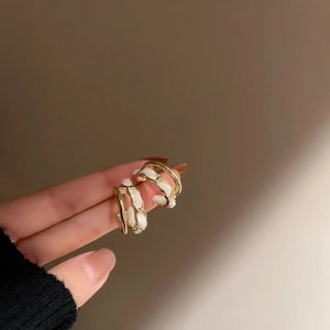 Detail of gold C-shaped earring with white woven leather chain on ear display
