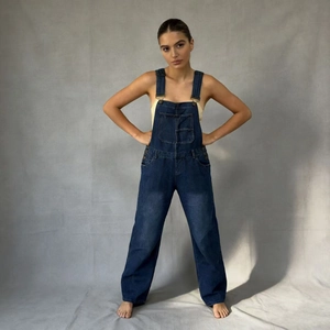 Detail view of dark blue denim overalls featuring adjustable metal buckles and chest pocket