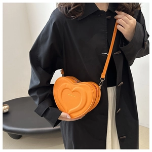 Detail view of orange heart-shaped crossbody bag with gold fashion text and adjustable strap