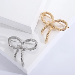 Close-up of twisted rope texture bow brooches in gold and silver finish on white stand