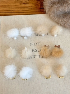 Macro detail of plush ball earrings with pearls and bows in white and khaki tones
