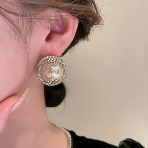Close-up of elegant gold circular earrings with pearl center and diamond halo