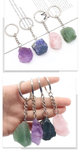 Detail of four natural raw stone keychains in green, purple, blue, and pink held by hand