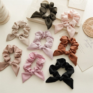 Close-up of elegant satin bow scrunchies in various colors on a textured stone background