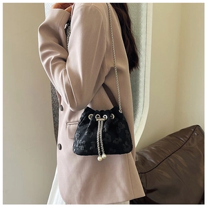 Detail of black drawstring bucket bag with floral texture and pearl chain strap