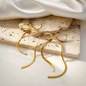 Detail view of 18K gold bow tassel earrings with snake chains on silk fabric