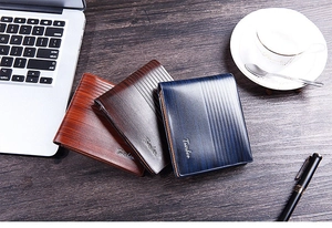 Three leather bifold wallets in brown and blue colors on a wooden office desk