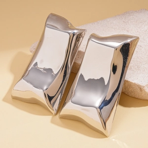 Close-up of irregular silver metallic earrings resting on a textured beige stone