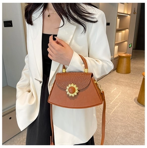 Details einer braunen Box-Tasche mit Kroko-Klappe und goldener Sonnenblumen-Schließe