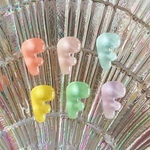 Close-up of matte resin F-shaped letter charms in vibrant colors on a glass shell