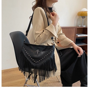 Détail d'un sac à bandoulière en cuir noir avec franges gothiques, rivets et pendentif croix