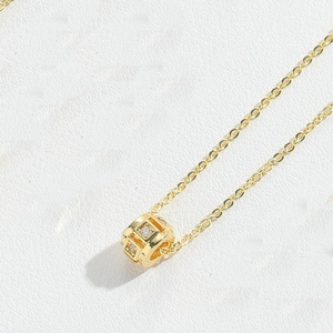 Close-up of a gold necklace featuring a hollow cubic pendant inlaid with white zircon