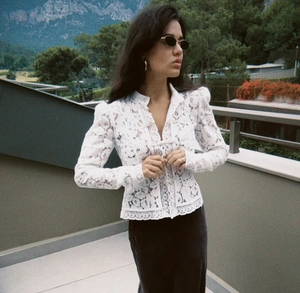 Detalle de blusa de encaje floral blanco con mangas abullonadas y cuello de estilo mao