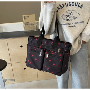Detail of black tote bag with cherry print and multiple zipper pockets on casual model