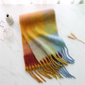 Flat lay of rainbow plaid tassel scarf on marble surface with decorative dry flowers