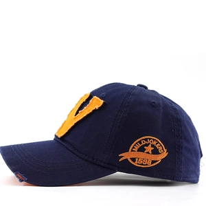 Détail d'une casquette en coton vieilli avec écusson orange en V et broderie latérale