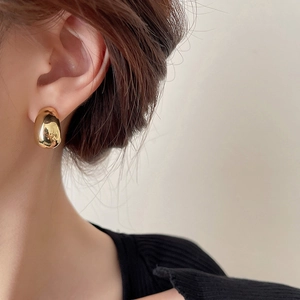 Detailed close-up of a gold water-drop earring worn on ear with polished finish