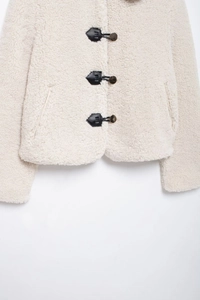 Dettaglio giacca beige in pile di agnello con bottoni dorati e finiture in pelle nera