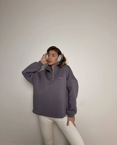 Detail of a dark grey half-zip sweatshirt featuring a pink 32 WEAR embroidered chest logo