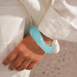 Close-up of light blue marble textured resin bangle on wrist with linen shirt