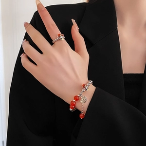 Detail of red bead bracelet and ring set with Ruyi lock pendant on a black blazer