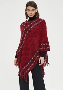 Detail of wine red knit poncho featuring colorful diamond patterns and long fringe trim